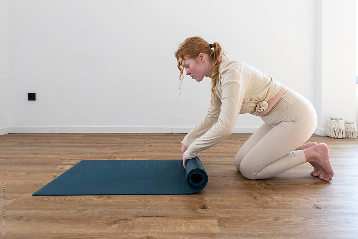 Young lady putting yoga mat on floor in studio
