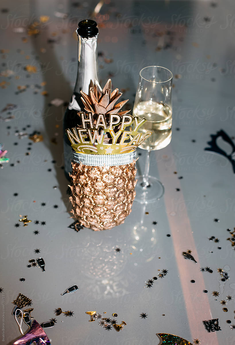 A bottle of champagne with a glass and a golden pineapple with happy new year headband