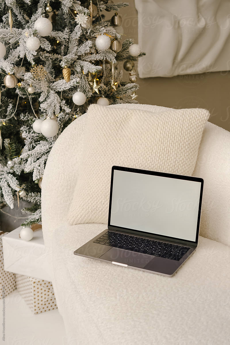 Laptop with blank screen placed on sofa near Christmas decorations