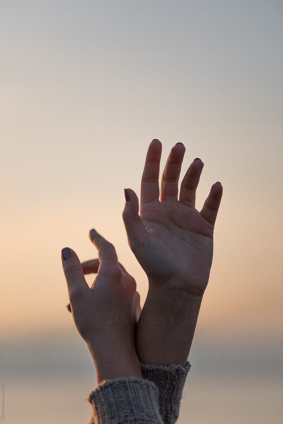 Famale hands raised against the sky at sunset