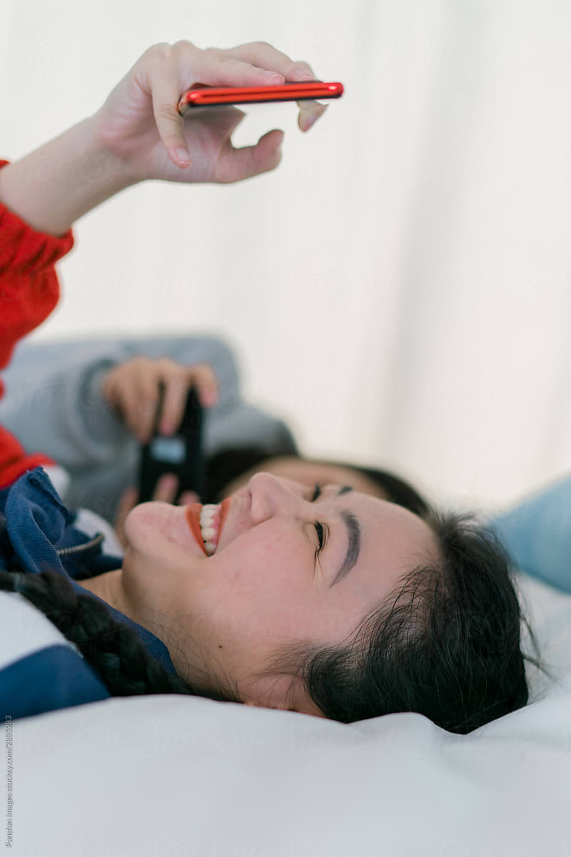 two young fashion asian female friends using cell phone on bed