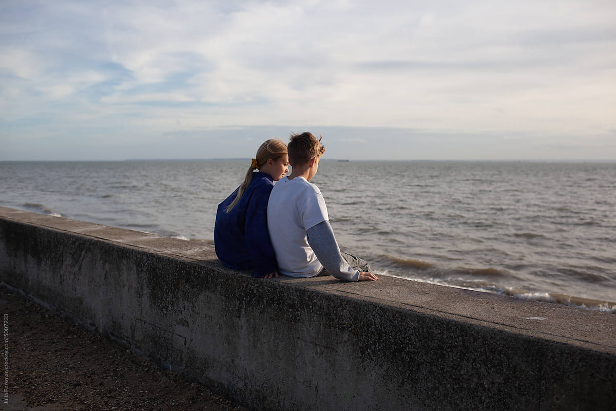 Children sit on a wall looking out to sea