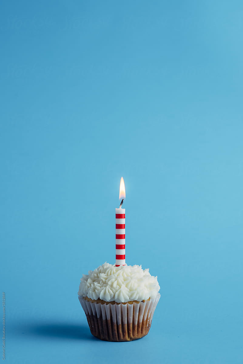 Cupcake with striped birthday candle on a blue background