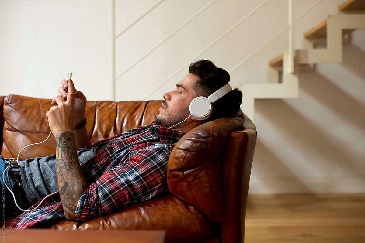 Man in headphones chatting on smartphone on cozy sofa
