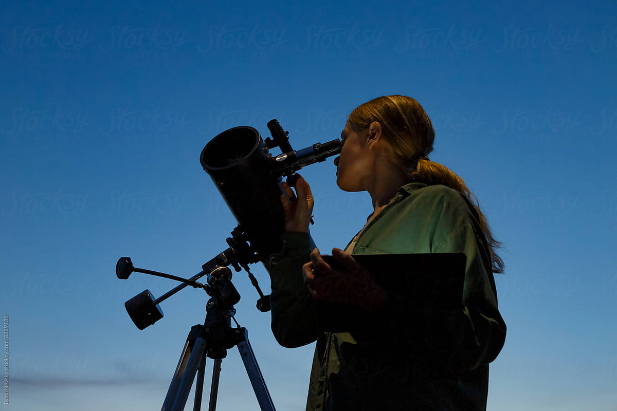 Woman with tablet using telescope against evening sky