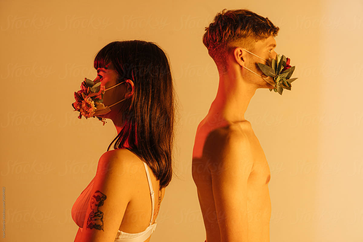 man and woman in flower masks stand with their backs to each other