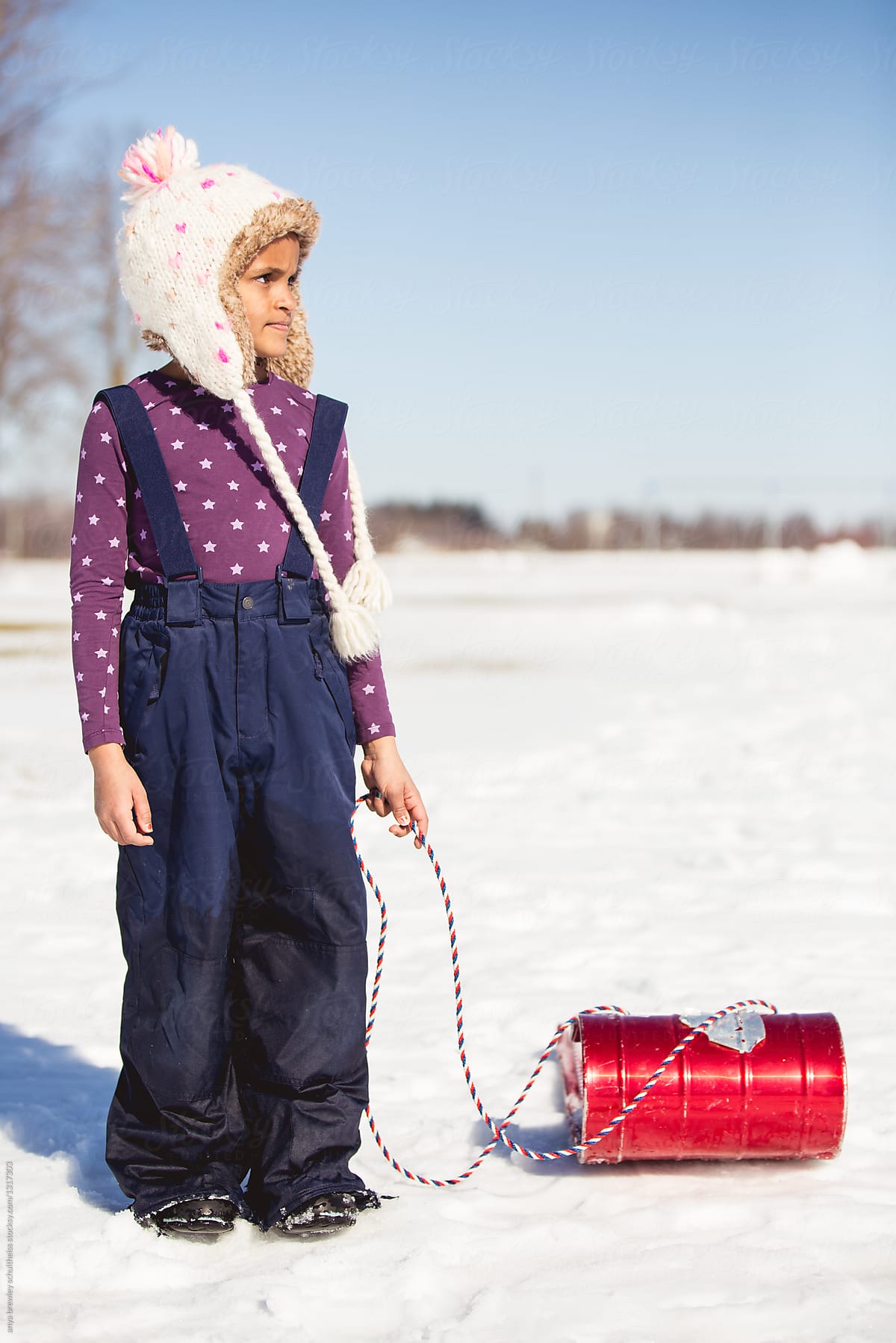 Young girl standing and holding her bright red toboggan