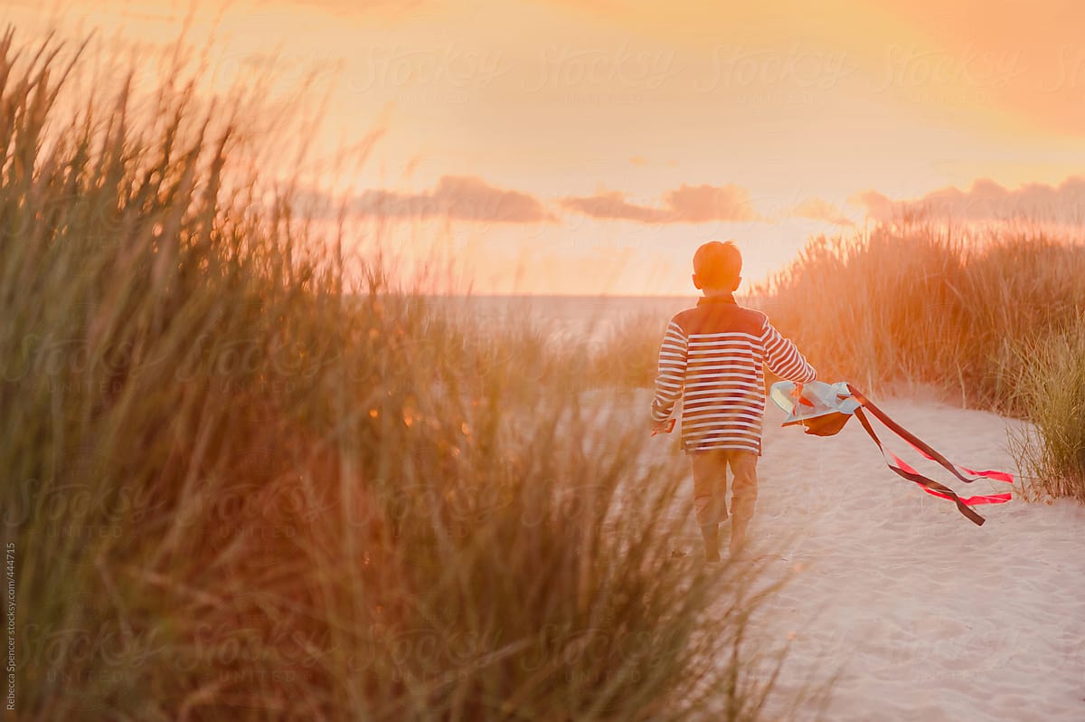 Boy walks into the sunset holding a kite