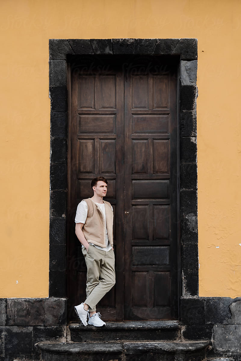 Young male leaning on door of old house