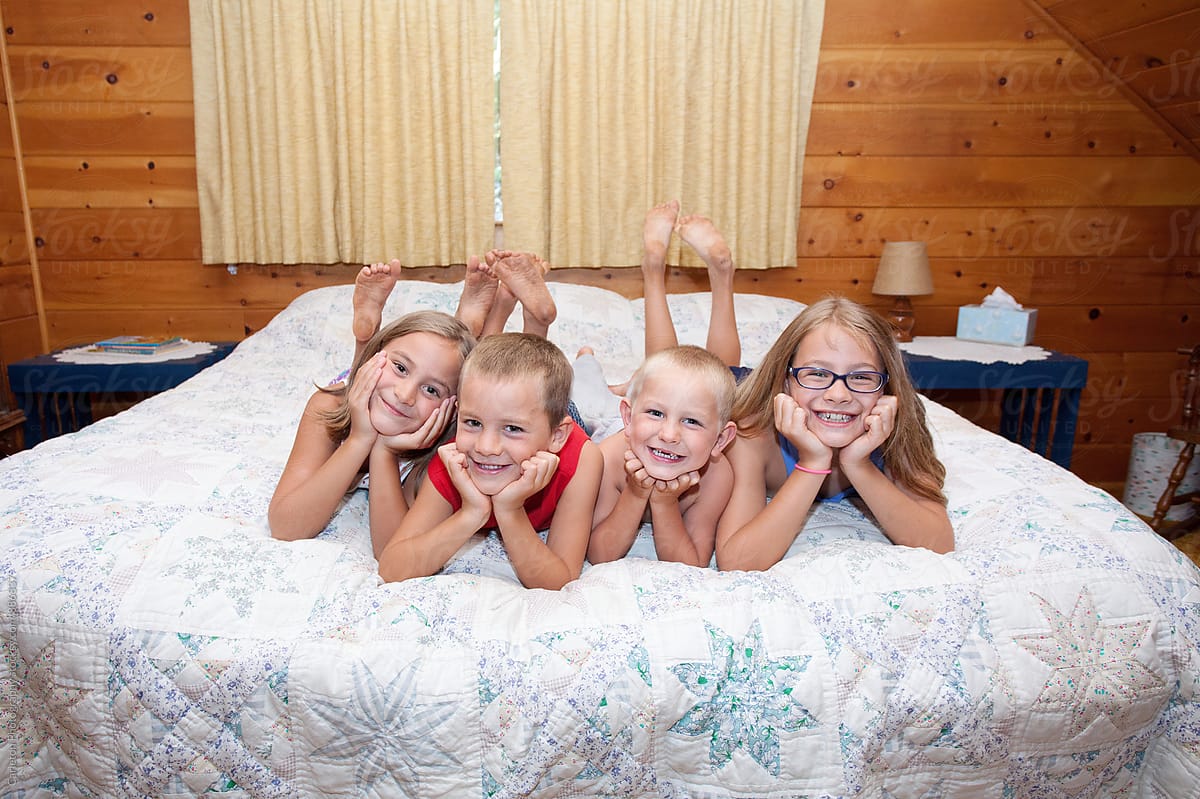 Four siblings on a bed in a wood paneled bedroom