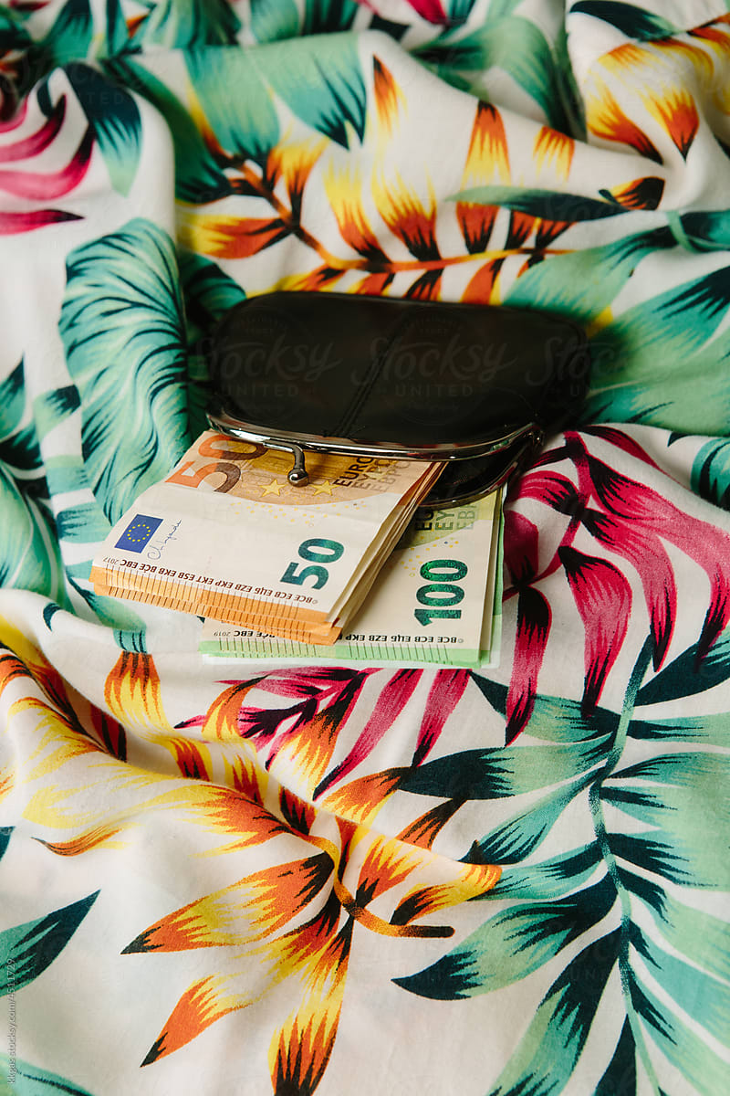 Purse filled with money, on a tropical fabric background