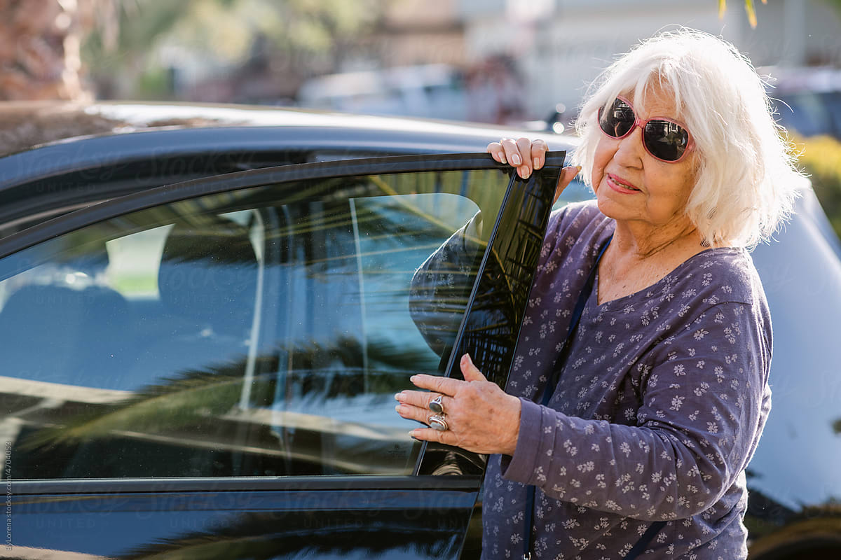 Senior fashion woman opening car door at city