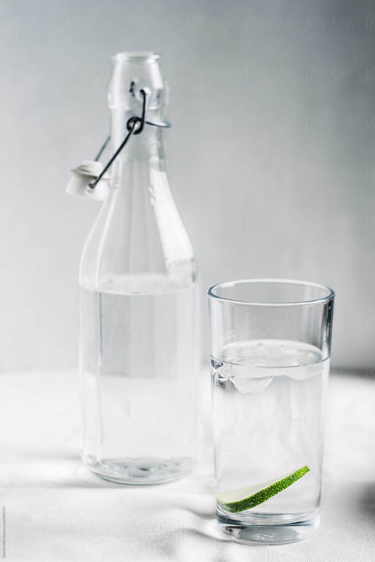 Glass and bottle of water on off white background.