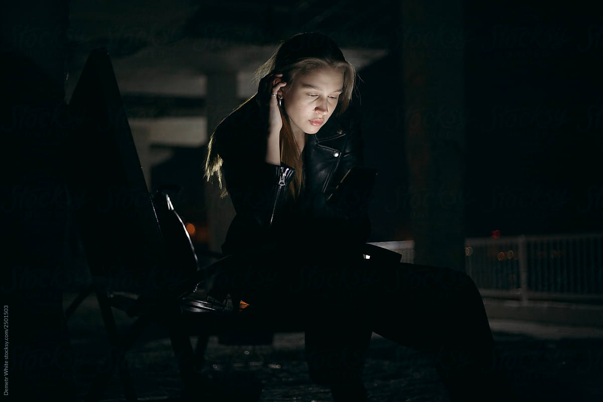 girl in a leather jacket sits in the dark and looks into the phone