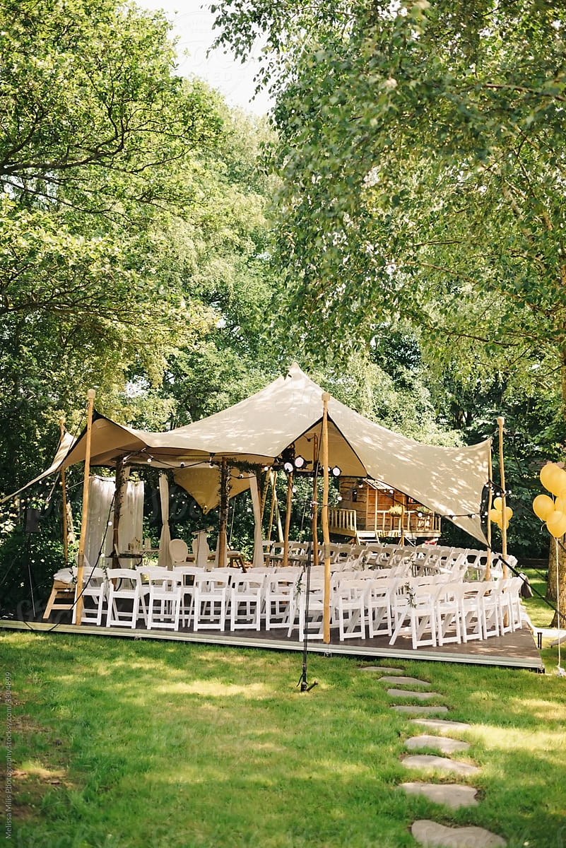 Wedding ceremony in the garden with white folding chairs and tent