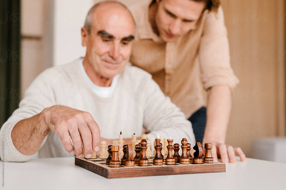 Happy senior man with son playing chess at home