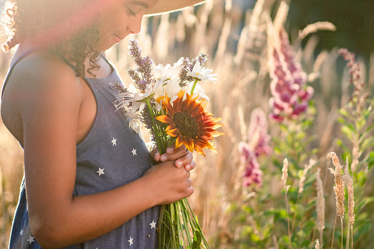 Girl in sundress and straw hat holding flowers with eyes closed