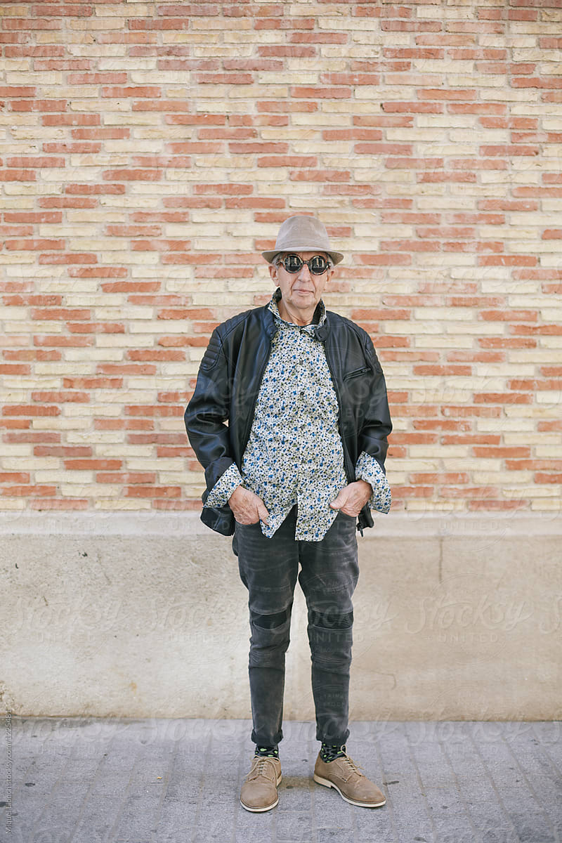 Full lenthg portrait of senior man standing in front of a brick walll