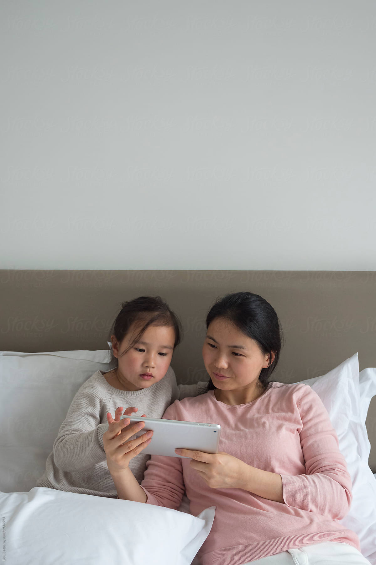 Little asian girl with her mother in bed using tablet