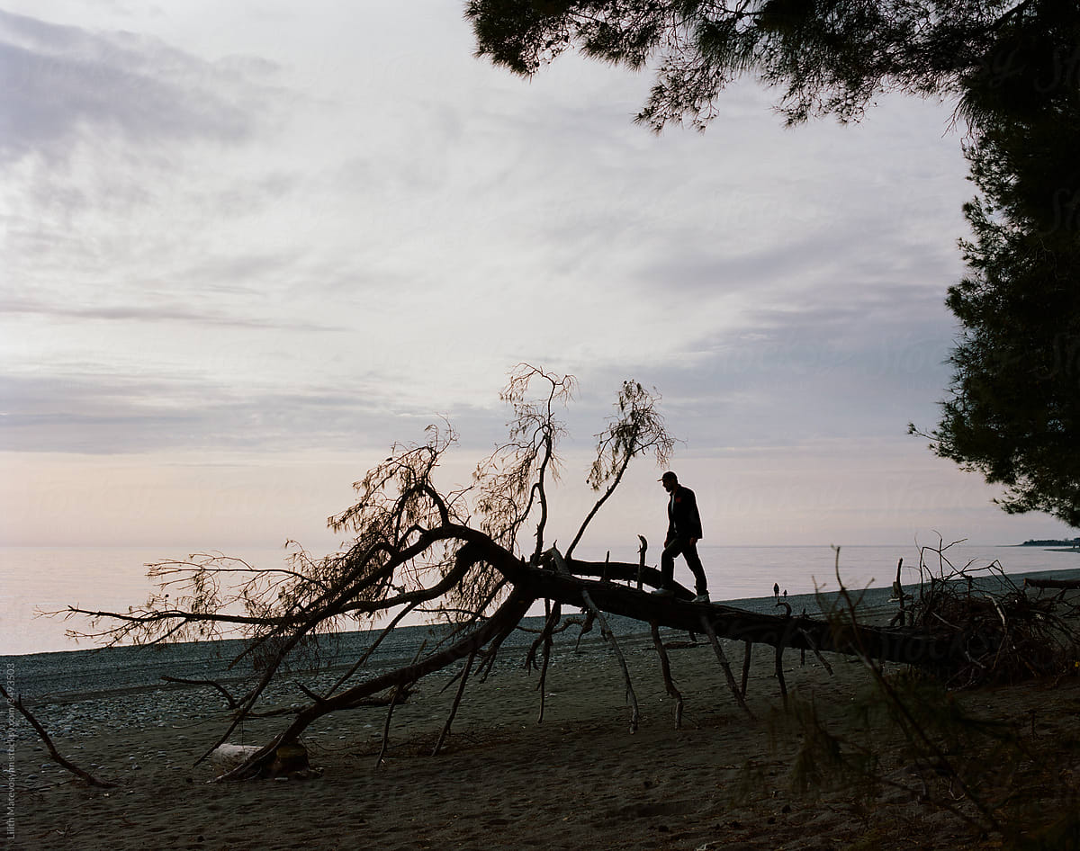 A Man Standing On The Tree Against The Black Sea