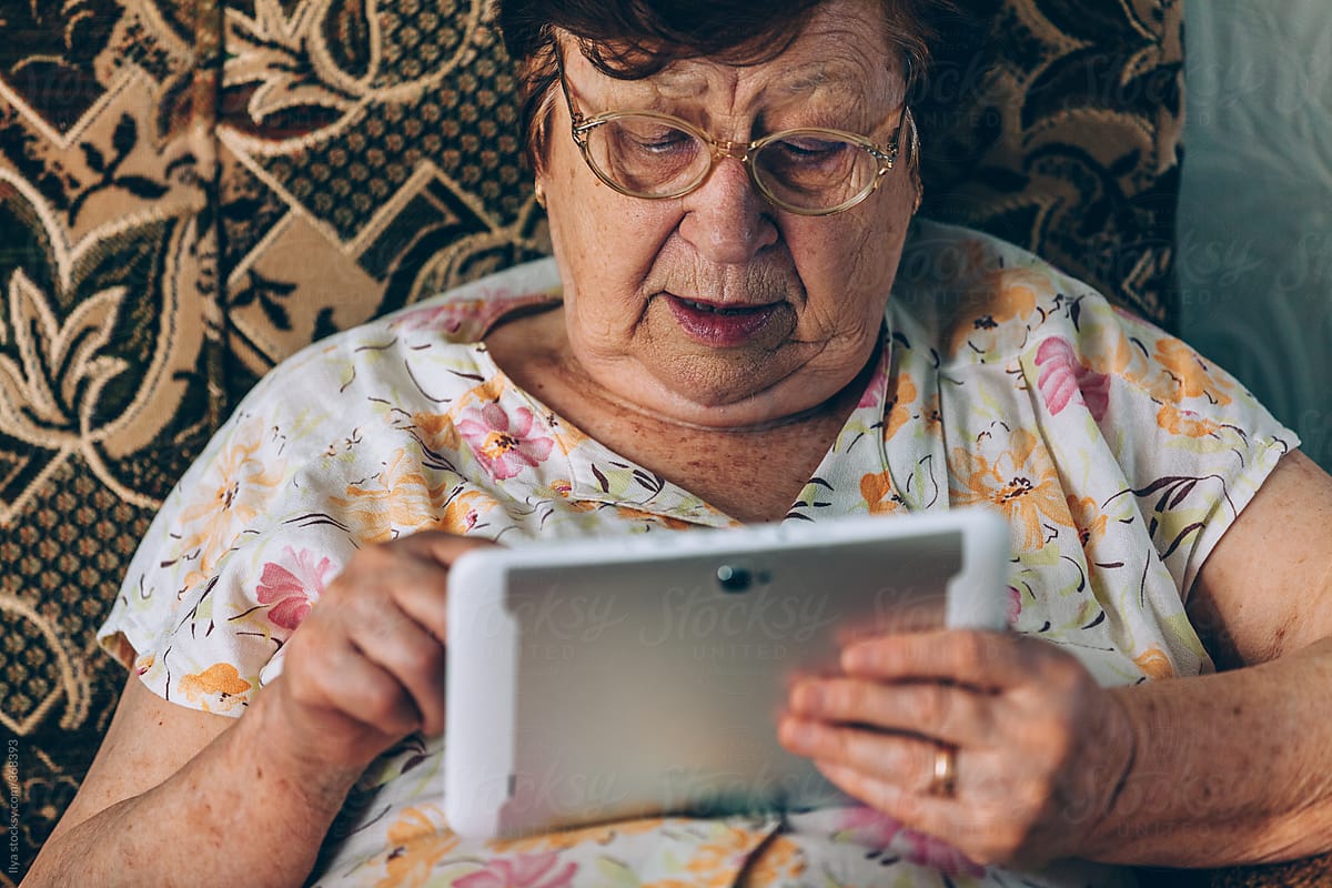 Old woman using tablet sitting at home