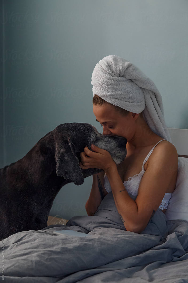 Woman kissing dog on bed