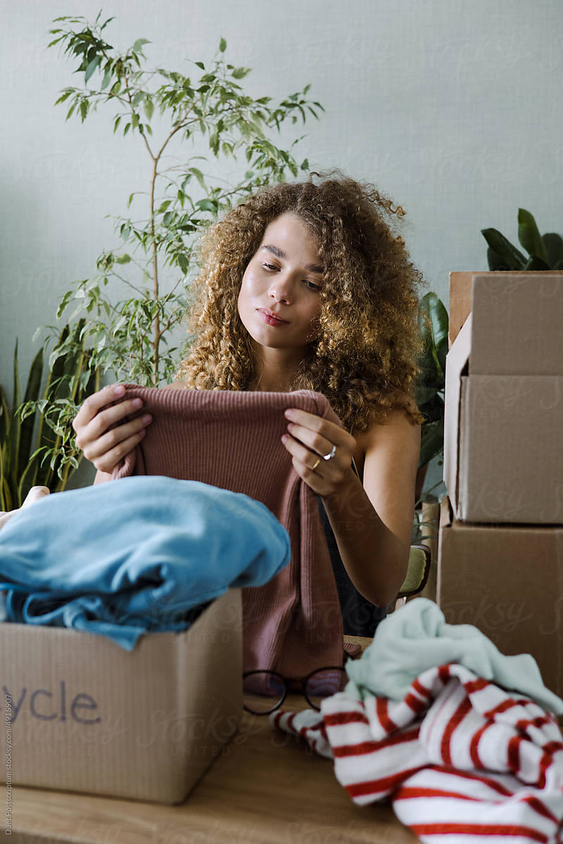 Curly young woman packing old clothes for recycling