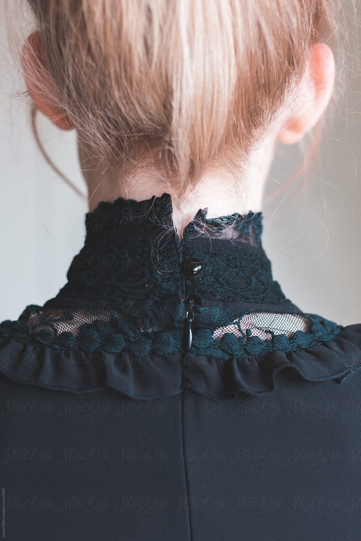 Back view of girl with blonde hair wearing a high collared black lace shirt