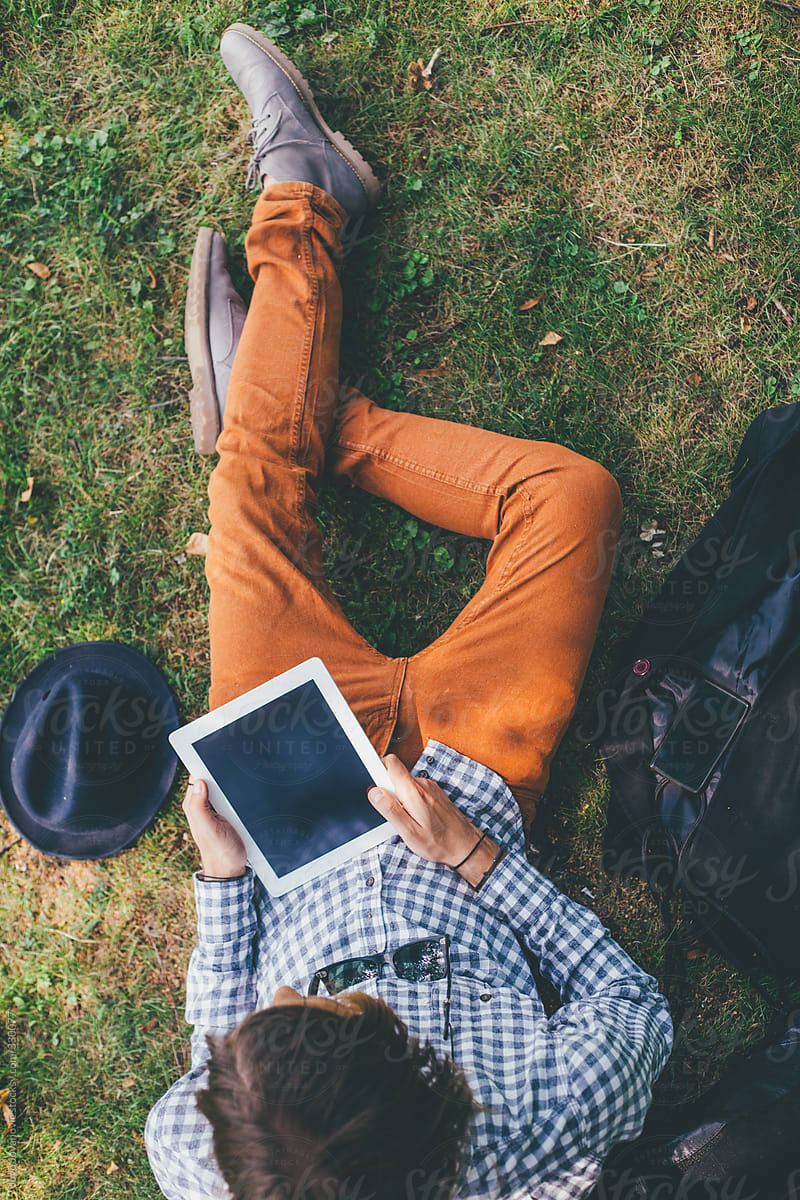 Young Man Using Tablet While Sitting On The Grass Overhead View By