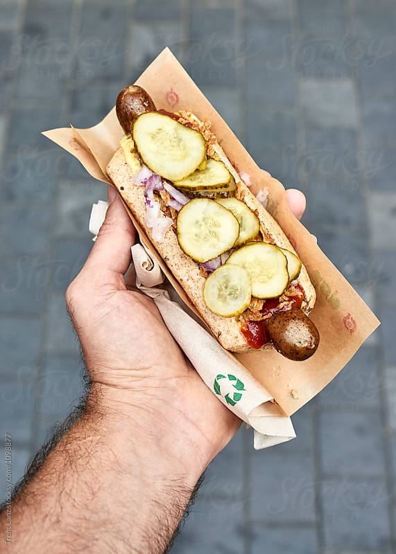 Hand holding hot dog against sidewalk