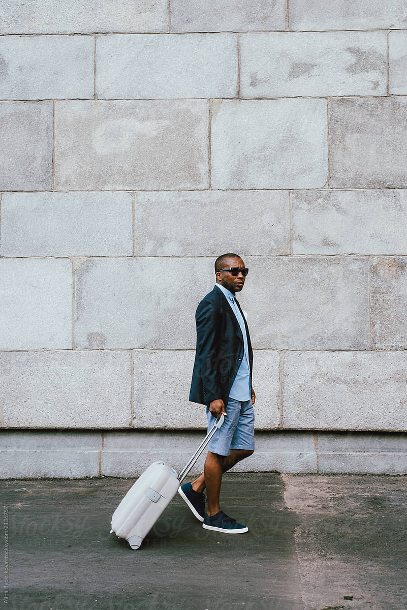 Black man with suitcase near brick wall
