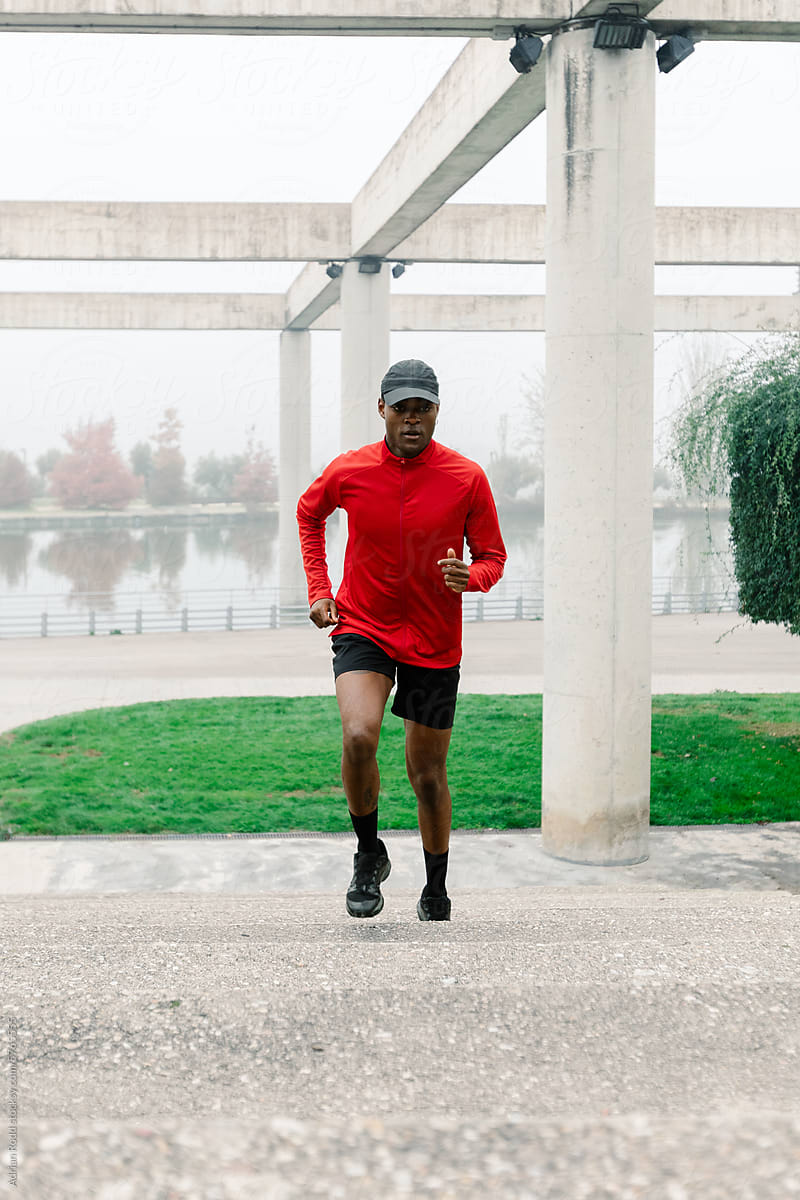 A black man in sports clothes trains in the morning in a public park