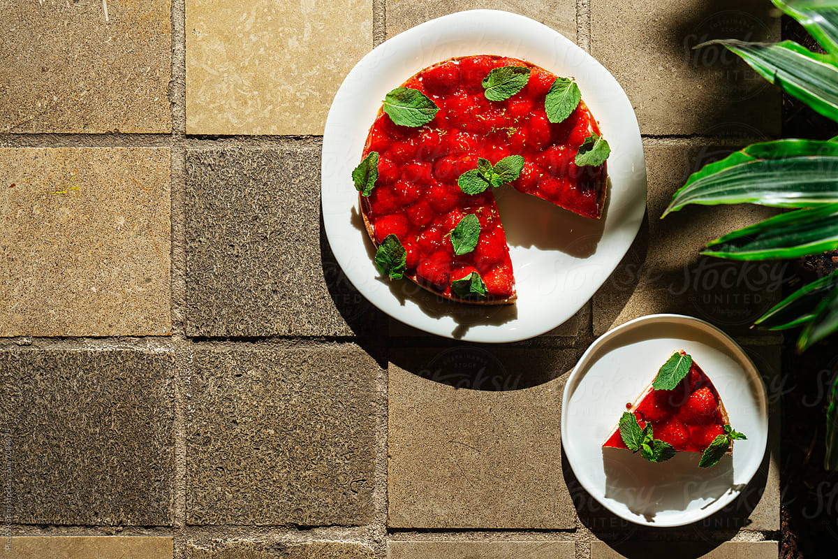 "Whole strawberry tart with one slice served on side plate" by Stocksy Contributor "Pietro Karras"