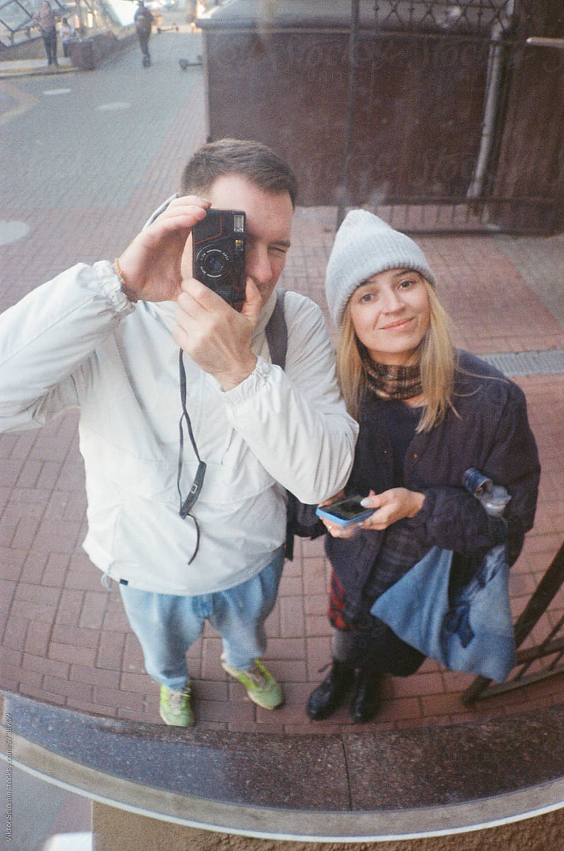 Cheerful couple taking photo on camera on street