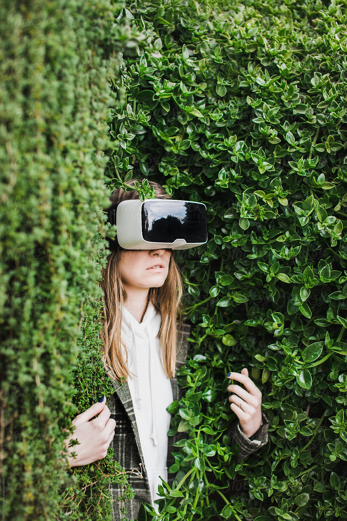 Blond girl in VR headset trapped in a green hedge