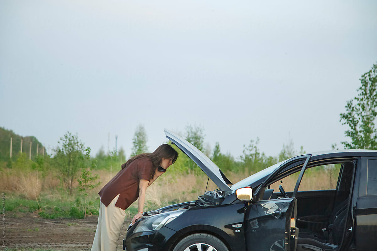 Female driver examining broken car during phone call