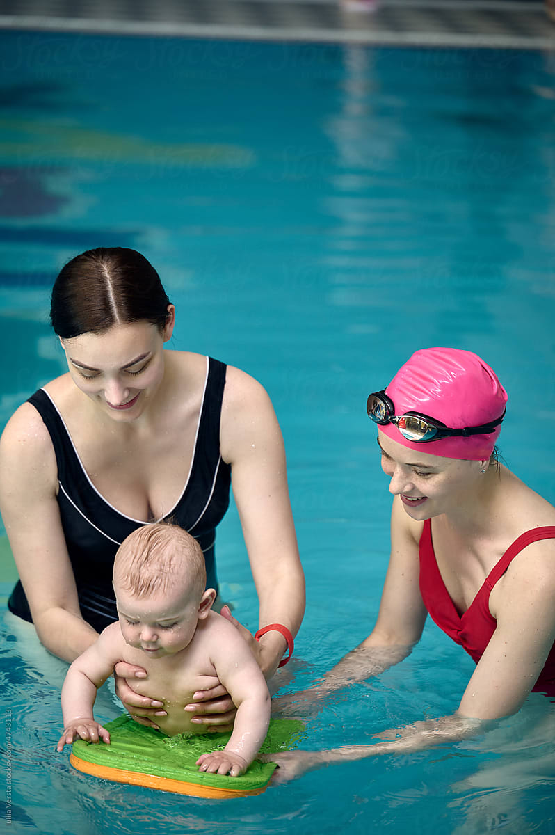 mother with a swimming coach teaching a baby to swim