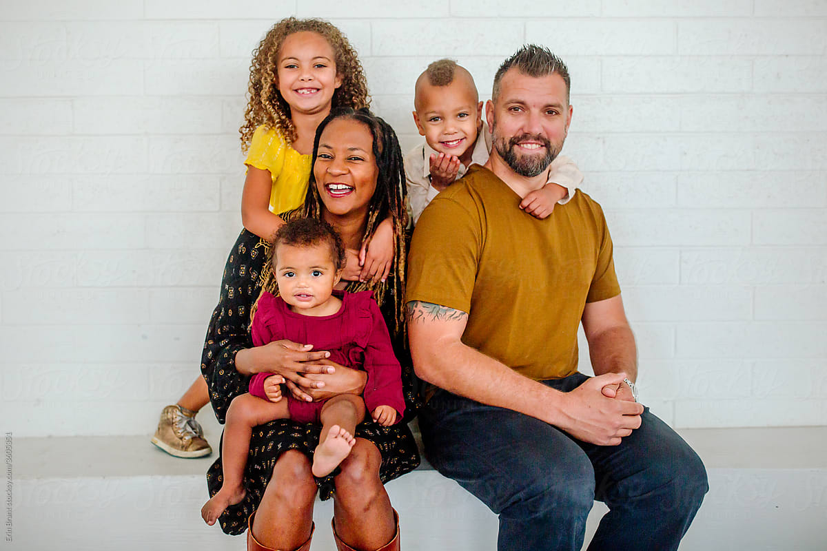 Biracial family seated on ledge in front of white wall