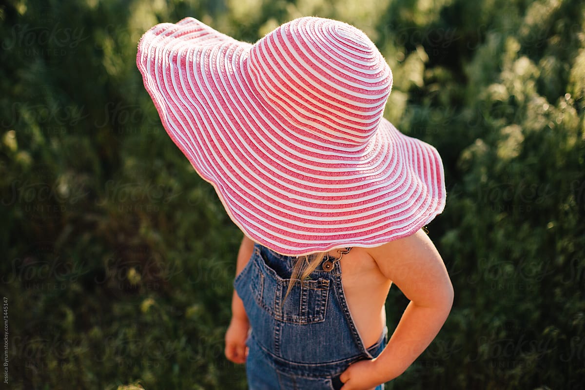 Toddler Girl In Denim Overalls And A Big Sun Hat. by Stocksy