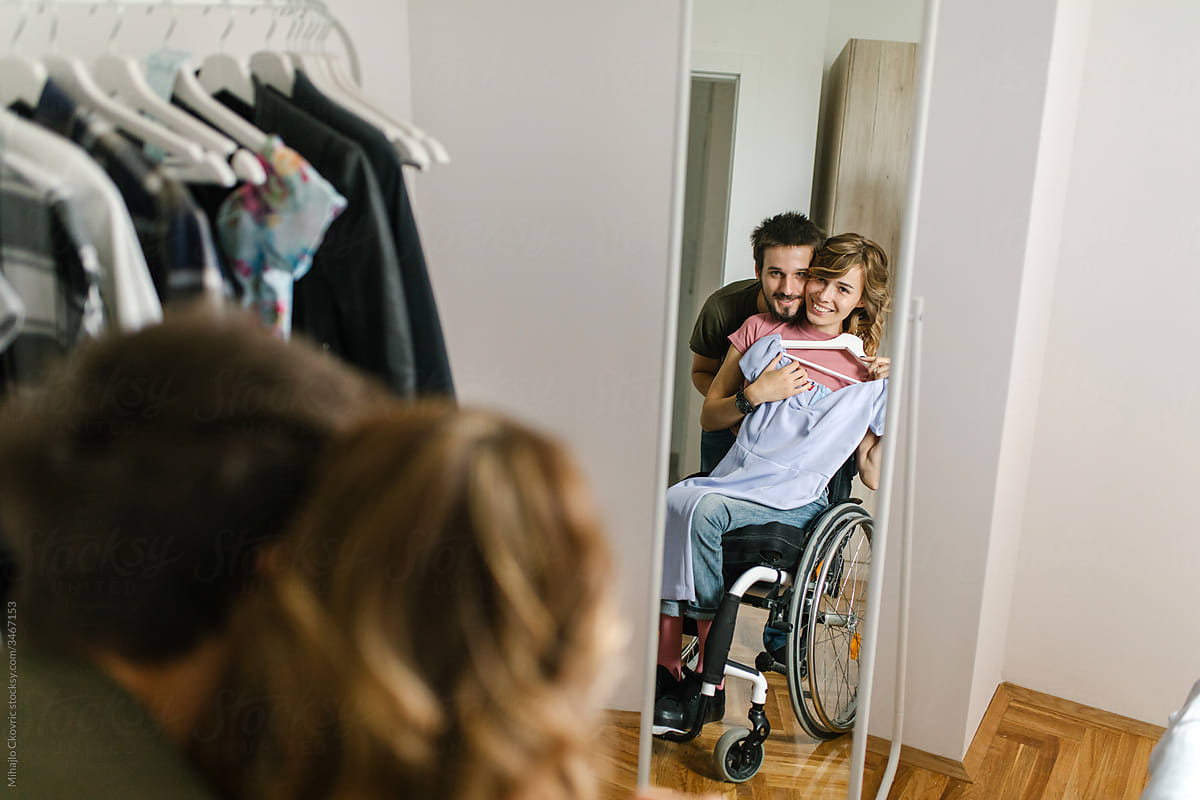 Young woman in a wheelchair choosing clothes from a clothes rack in her bedroom