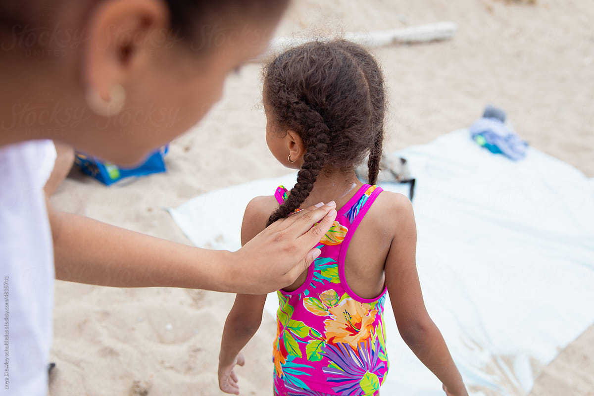 Teen applying sunscreen to her sisters back and shoulder