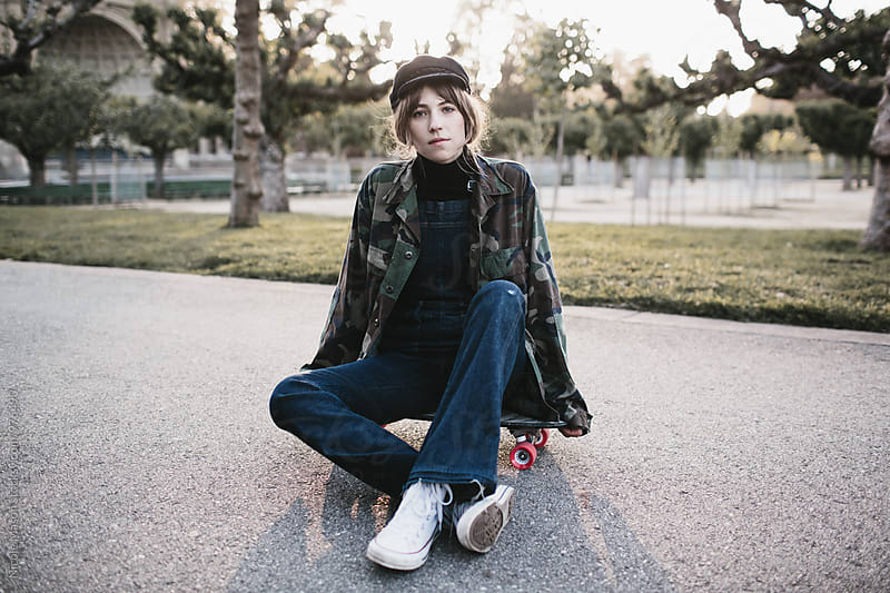 young woman sitting on skateboard in park at sunset