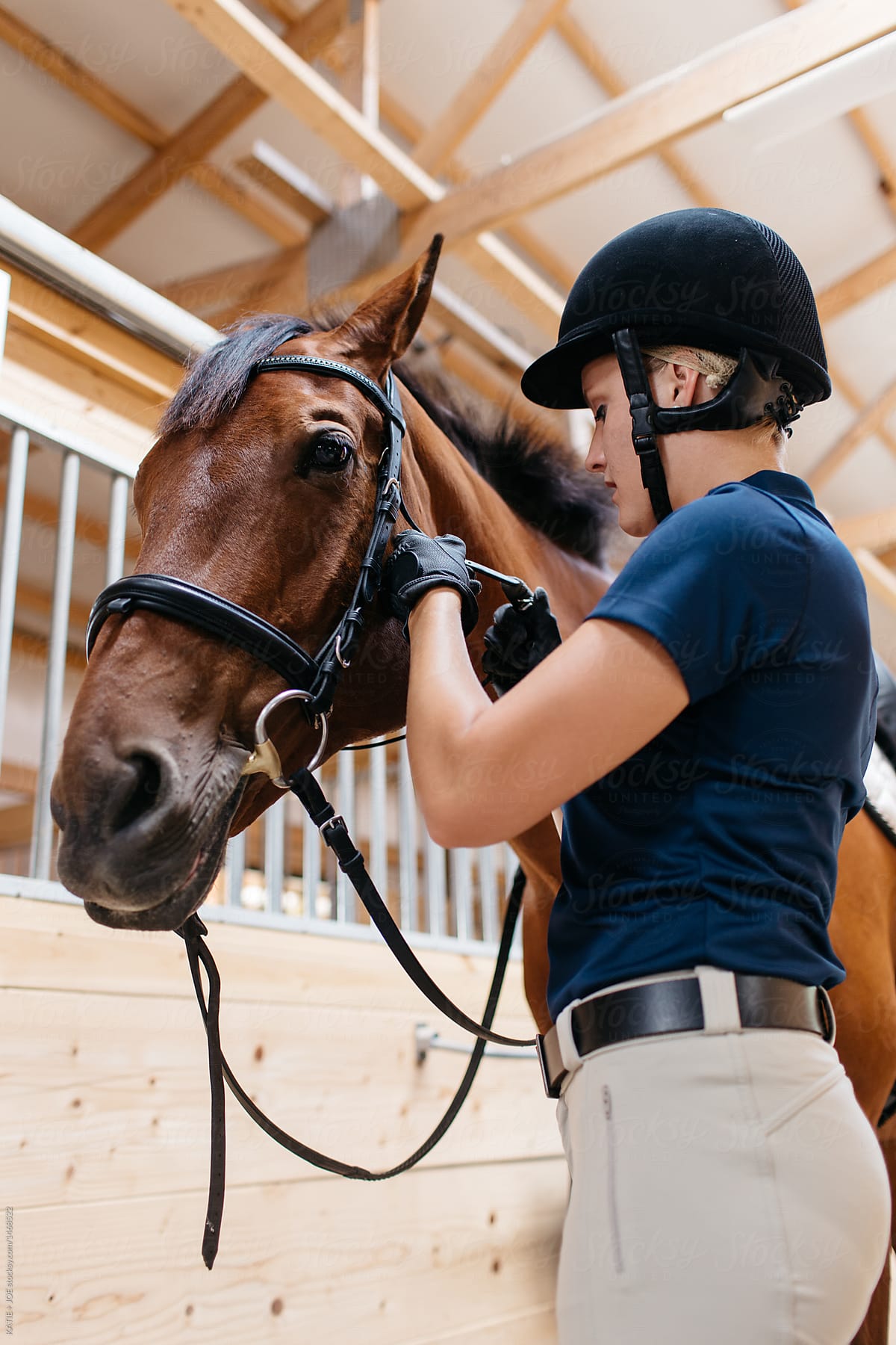 Young woman rider tacking up her horse in a barn