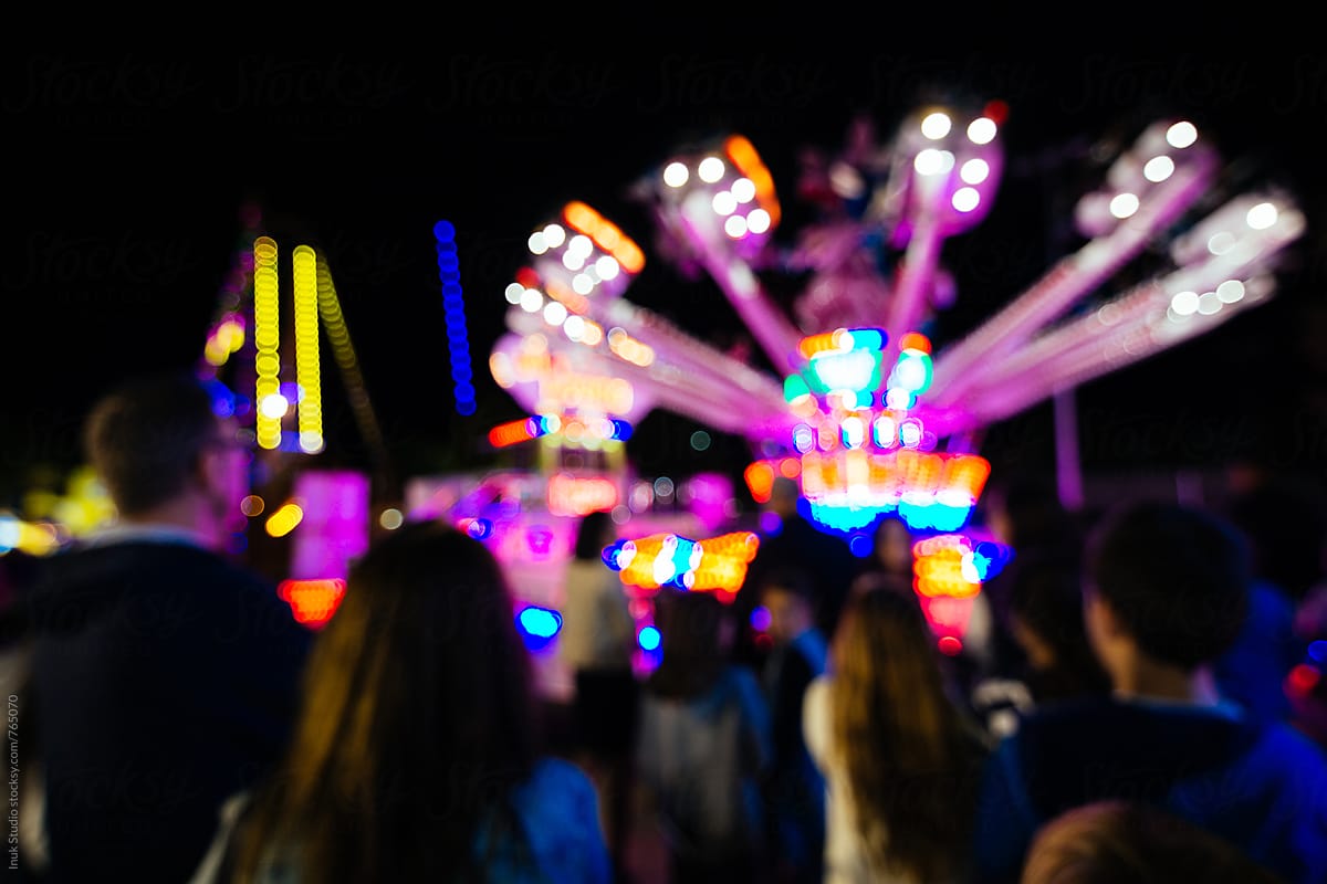 Blurred scene of people in a fair at night with colourful lights and attractions