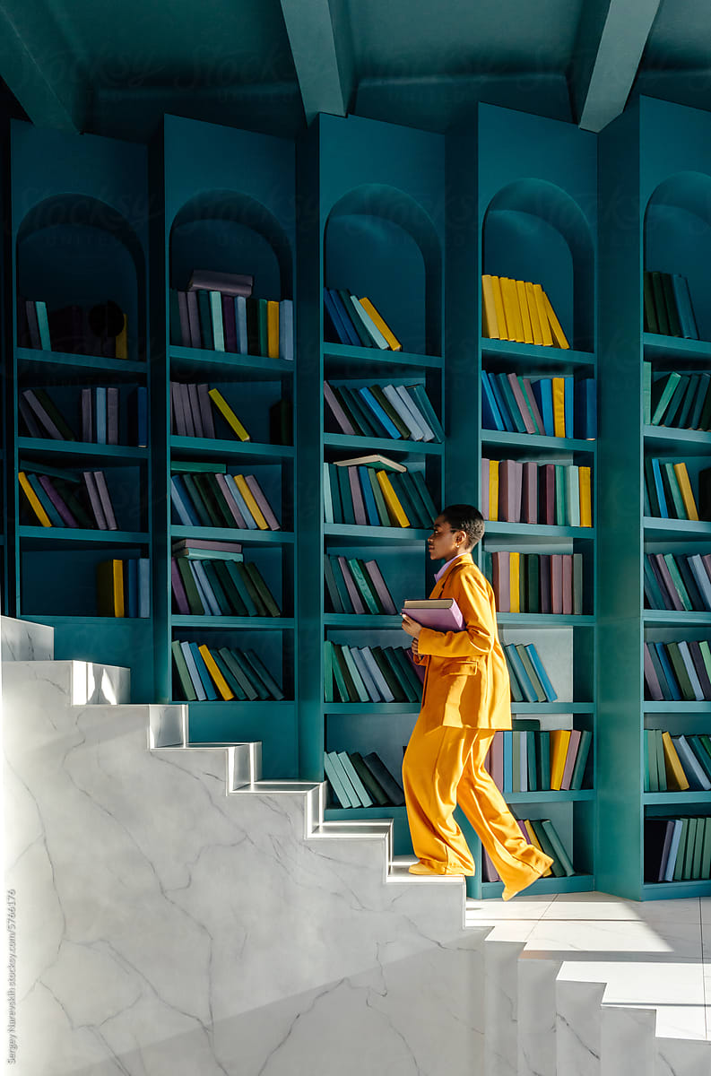 Woman in yellow suit climbing on stairs in room with book shelves