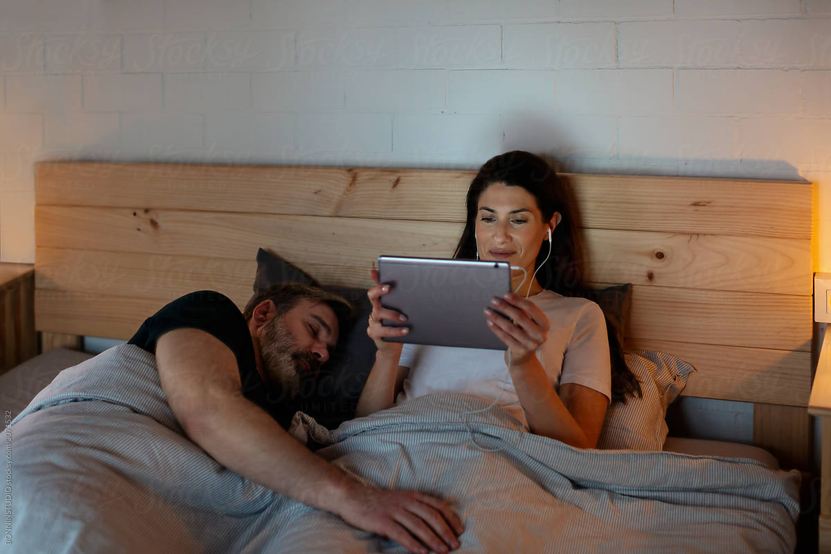 Sleeping mature man hugging wife with tablet in bed
