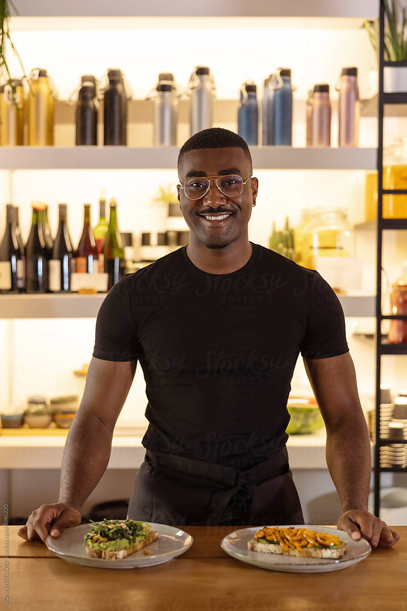 Cheerful black male cook standing with food at counter in cafe