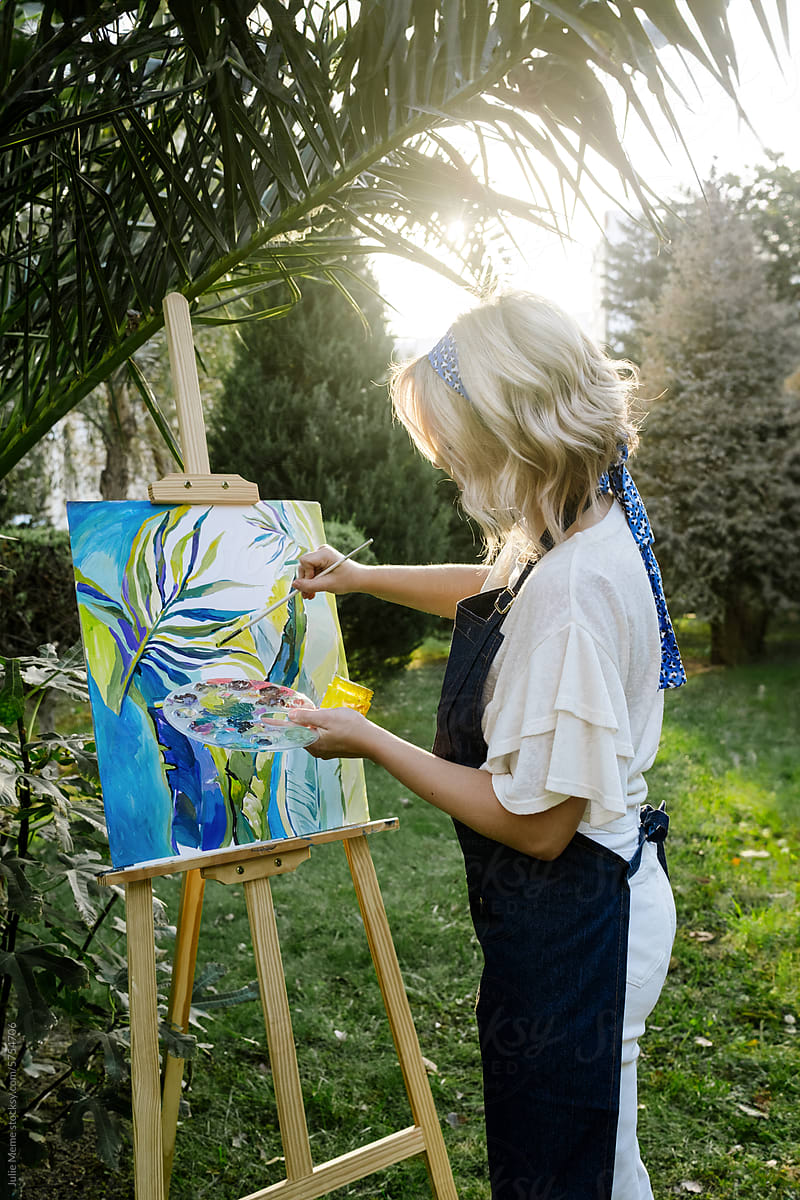 A blonde artist stays in the sunlight while painting nature