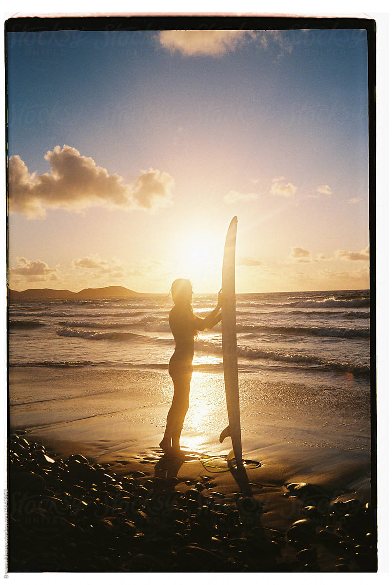 woman on black sand beach with her surfboard