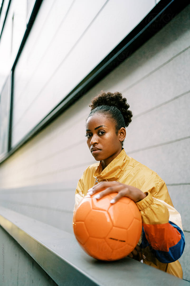 Serious female footballer standing with ball in street